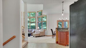 A spacious living area with large windows, a cozy seating area, and a kitchen with wooden cabinets. - Walk to Holiday Valley, Family-sized House, Sleeps 9, Shuffleboard, 2 fireplaces (Ellicottville)