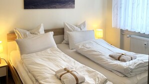 Two single beds with white linens and towels, bedside lamps, and a painting on the wall. - Winterberg gem With Pool, Sauna (Winterberg)