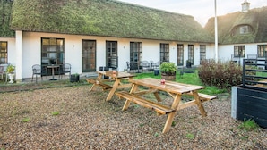 A building with a thatched roof, numbered rooms, outdoor seating, and a gravel courtyard.