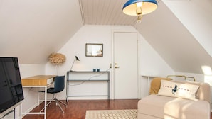 A compact room with a wooden desk, a chair, a sofa with a cushion, a patterned rug, and a ceiling light fixture.