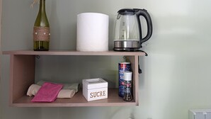 Een plank met een fles wijn, toiletpapier, een waterkoker, een doosje met de tekst 'SUCRE', een blikje frisdrank en een peperfles.