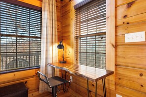 A corner room with wooden walls, a desk, a chair, and a window with blinds.