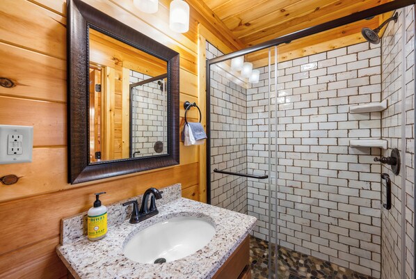 A bathroom with a wooden interior, a granite sink, a mirror, and a shower with white tiles.