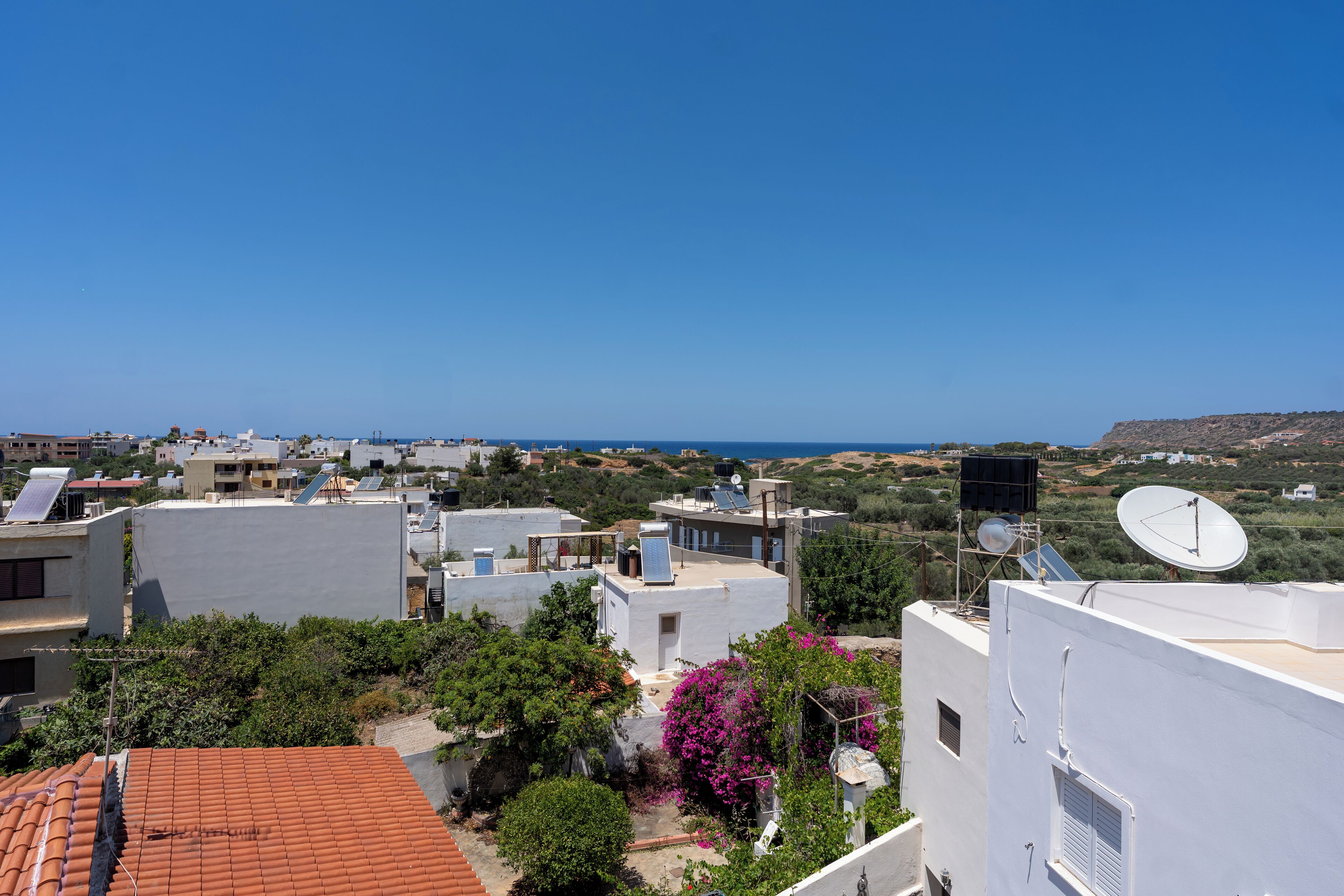 Zona residencial con edificios, cielo azul despejado y vista distante del mar.