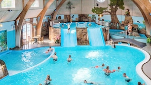 Una piscina interior amb diverses línies de bany, un tobogan i una zona de seients amb taules i cadires.