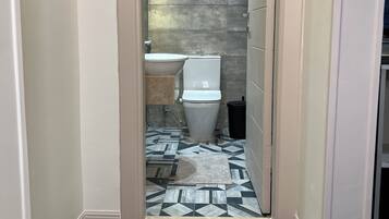 A narrow hallway leading to a bathroom with a tiled floor, a white toilet, and a mounted air conditioning unit.