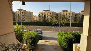 A residential area with a paved driveway leading to a gated entrance, surrounded by greenery and modern apartment buildings. - 6th Of October Signature Stay (6th of October City)
