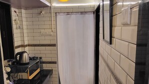 Una cocina estrecha con paredes de azulejos blancos, encimera negra y lámpara colgante negra.