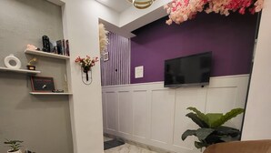 Una sala de estar moderna con un sofá, una mesa de centro y un televisor montado en la pared. Hay una planta decorativa y un jarrón en un estante.