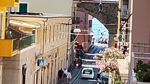 Une rue étroite bordée de bâtiments des deux côtés, un pont en arrière-plan et des voitures garées.