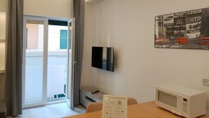 Una habitación de hotel moderna con un ventanal corredero que da a un balcón, un televisor de pantalla plana en la pared y un microondas sobre la mesa.