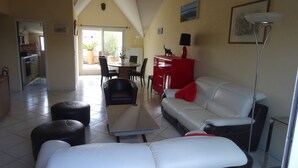 A living room with a white sofa, black and white ottoman, and a dining area with a table and chairs.