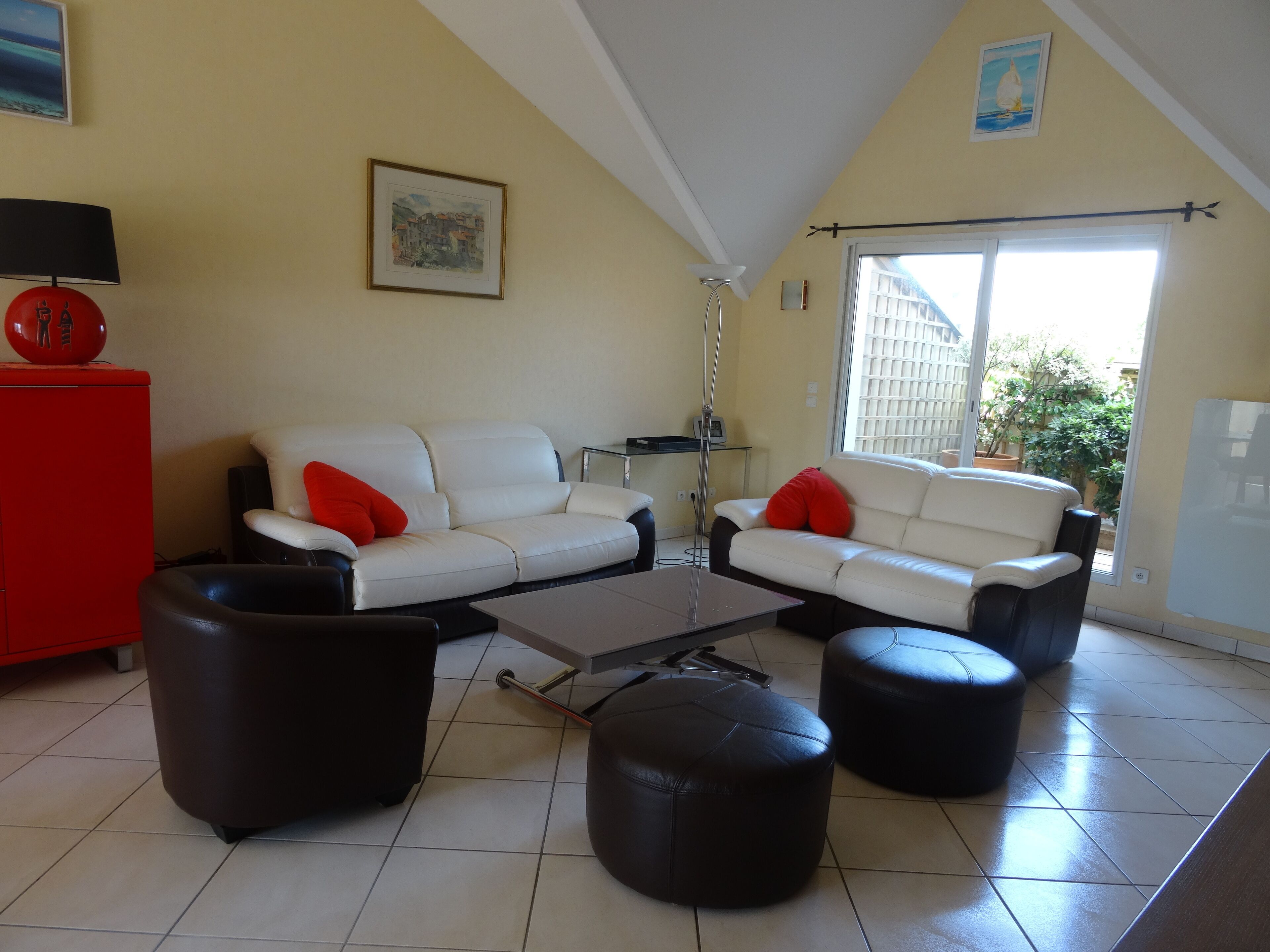 Un salon avec un canapé blanc, des poufs noirs, un meuble rouge et un ventilateur de plafond.
