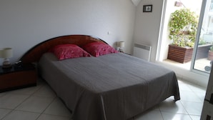 A bedroom with a bed, nightstands, a lamp, a radiator, and a view of the outside.