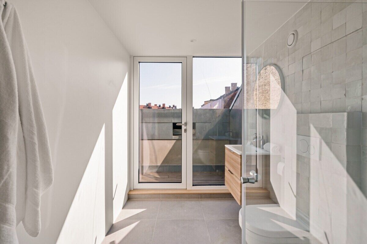 A modern bathroom with a glass shower enclosure, a wooden cabinet, and a view of the cityscape through the glass door.