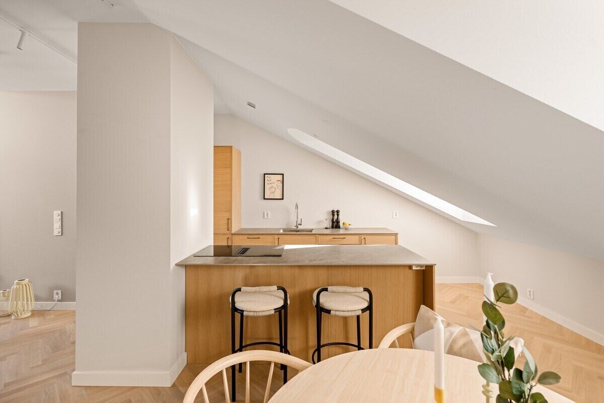 A modern kitchen with a central island, wooden bar stools, and a dining table with chairs.