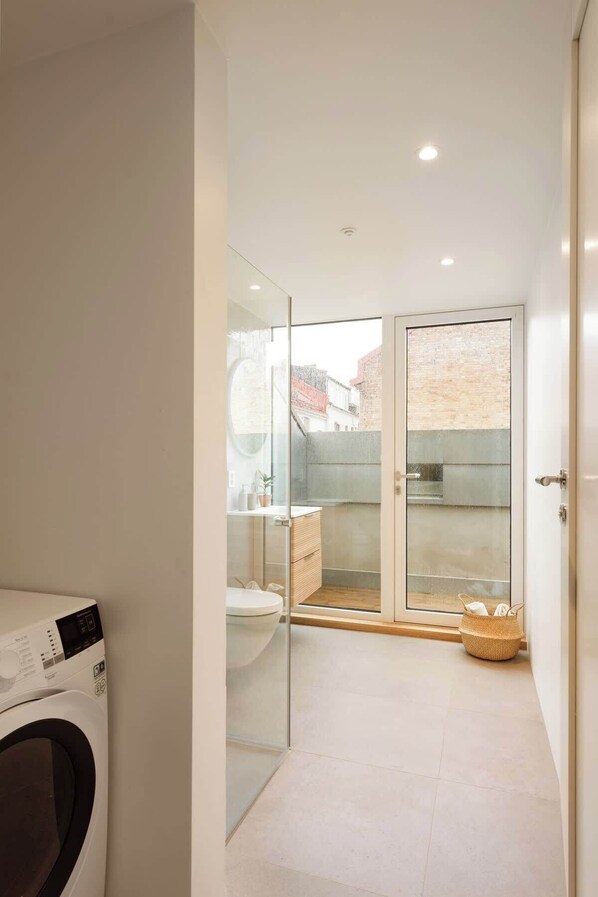 A compact, modern bathroom with a glass shower enclosure, a toilet, and a washing machine. - Dinbnb Apartments Grunerlokka (Oslo)