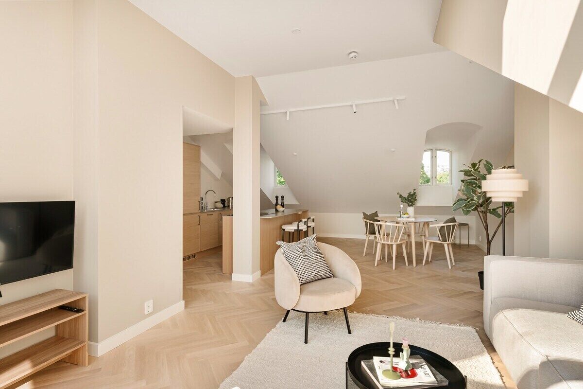 Un vaste espace de vie comprenant un téléviseur à écran plat, un canapé, une table à manger avec des chaises, et une cuisine à l’arrière-plan.