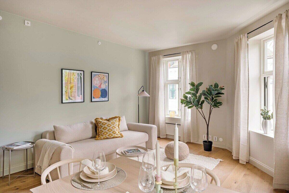 A modern living room with a sofa, dining table set for four, and a potted plant.
