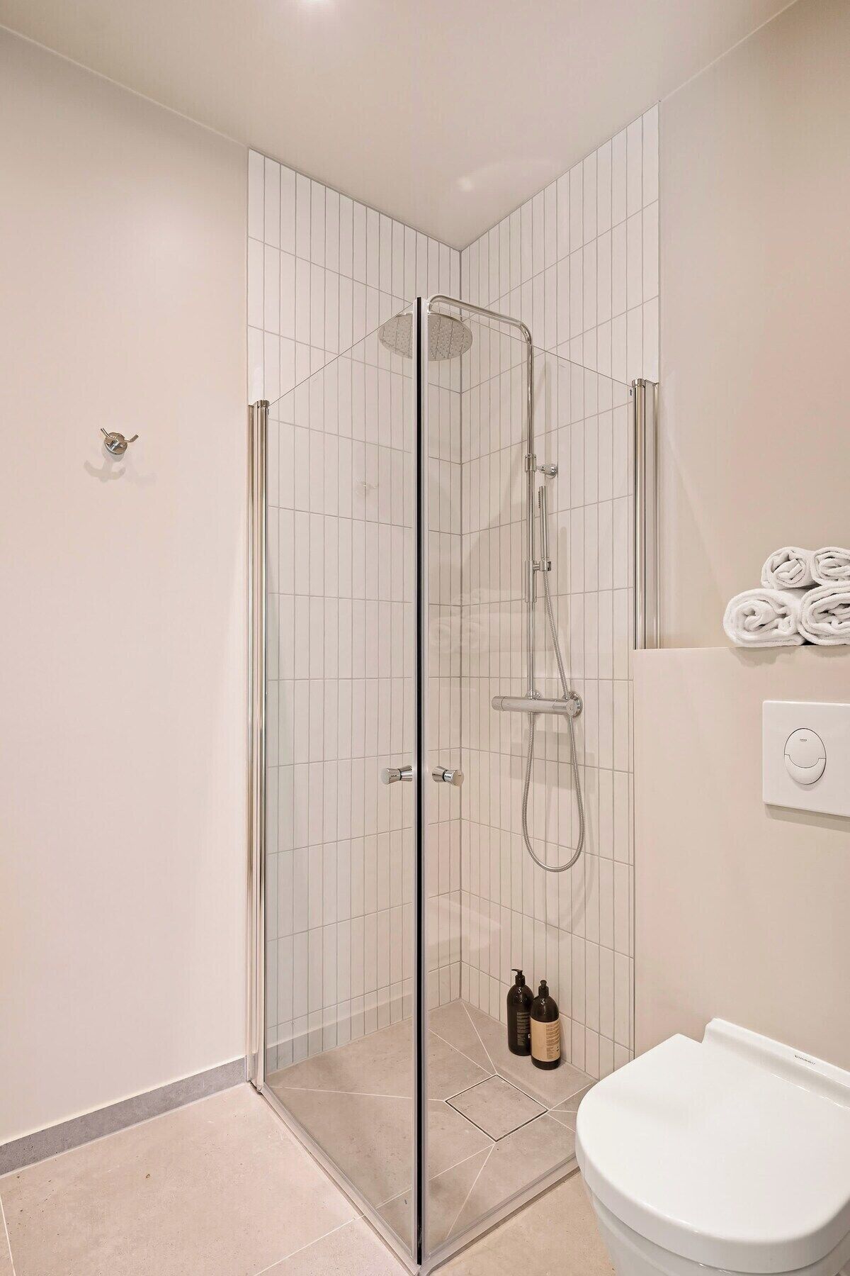 A modern bathroom with a glass-enclosed shower, a toilet, and a towel rack with towels.