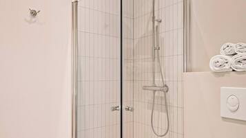 A modern bathroom with a glass-enclosed shower, a toilet, and a towel rack with towels.