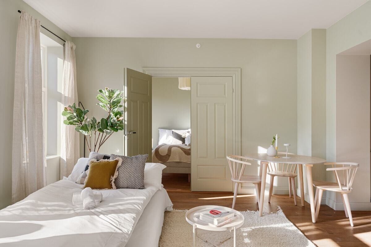 Een slaapkamer met een bed, nachtkastje en een kleine tafel met stoelen. Er is een deur die naar een andere kamer leidt.