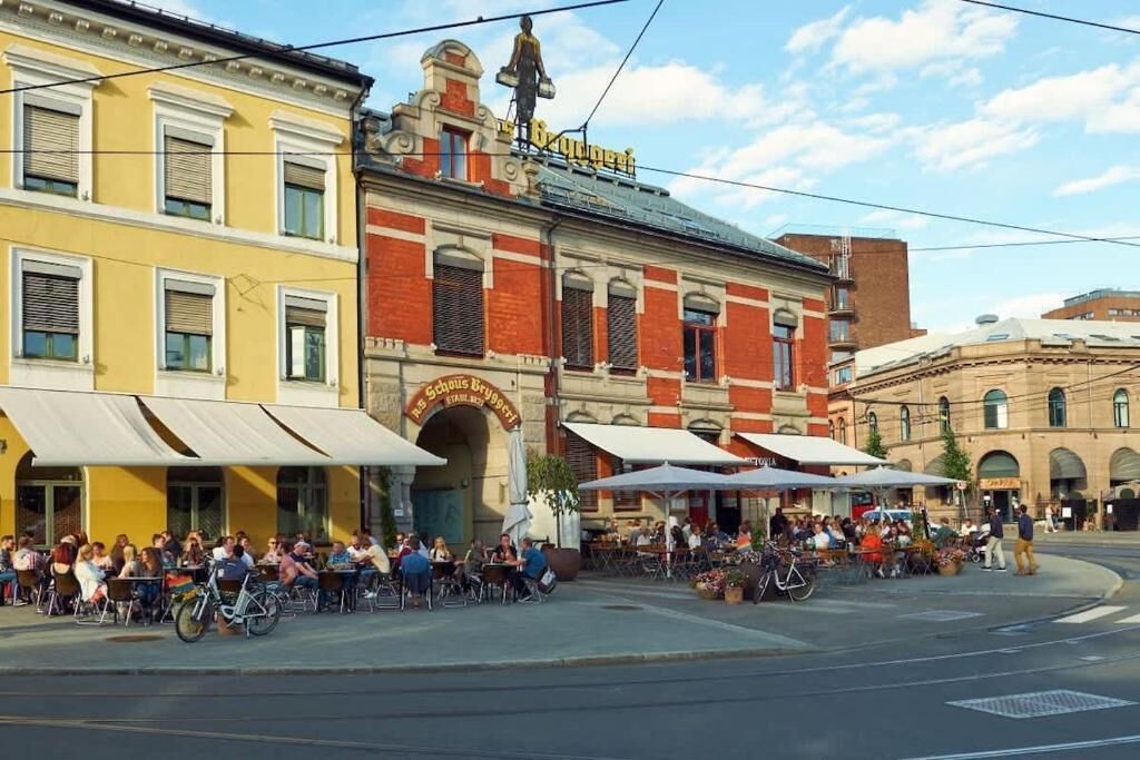 Une scène de rue avec des tables et des chaises installées à l’extérieur d’un restaurant dont la façade est en briques rouges et le bâtiment est jaune.