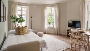 Un dormitorio con cama, televisor, mesa de comedor con sillas y ventana con cortinas.