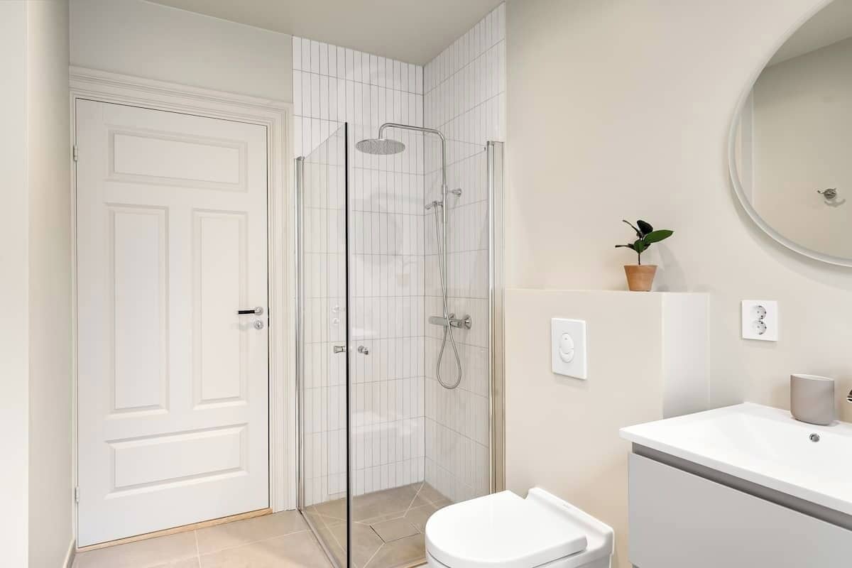 Een moderne badkamer met een douche met glazen wand, een wit toilet en een wastafel met spiegel.