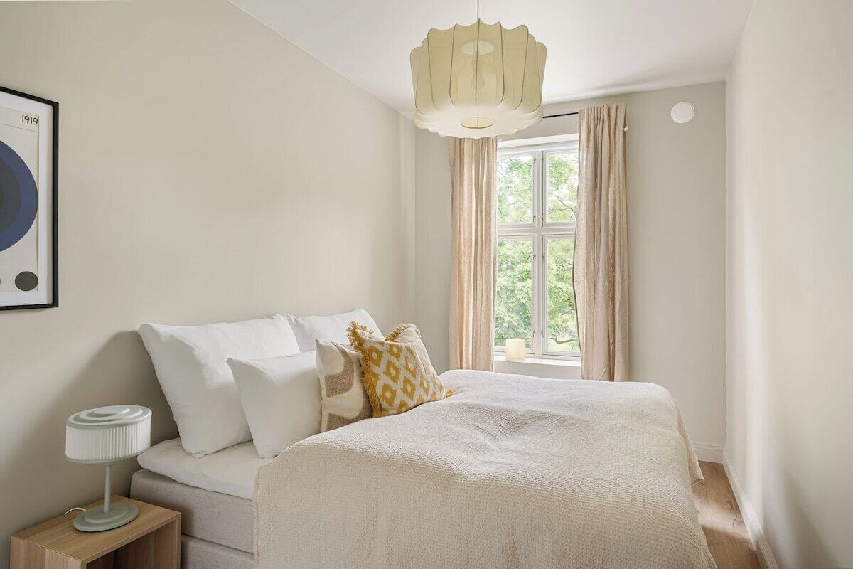 A bedroom with a bed, bedside table, lamp, and a window with curtains.