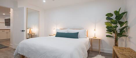 Un dormitorio moderno con una cama grande, mesitas de noche, un ventilador de techo y una planta en maceta.