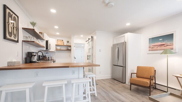 A modern kitchen with white cabinetry, a wooden countertop, and a stainless steel refrigerator. There are three white stools at the counter and a brown chair in the corner. - Boomerang 202: New remodel! (Telluride)