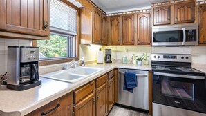 A kitchen with wooden cabinets, a stainless steel coffee maker, a microwave, and an oven.