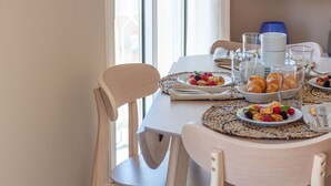 A dining table set with plates of food, glasses, and cutlery, with a chair visible on the left.