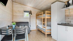 A compact room with a bunk bed, a small kitchenette, a dining area with a table and chairs, and a single window providing natural light.