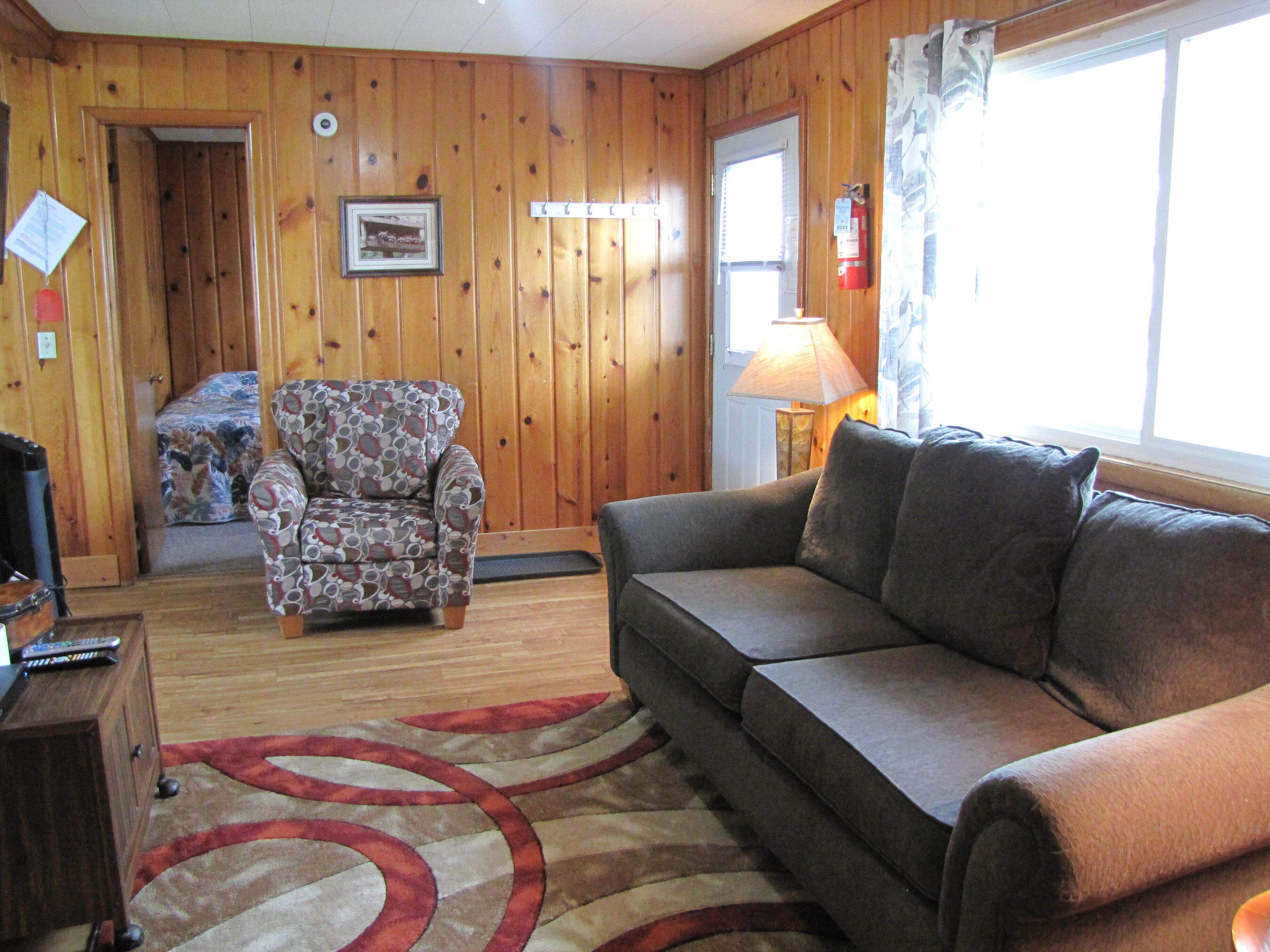 A wooden-paneled room with a sofa, armchair, and a rug.