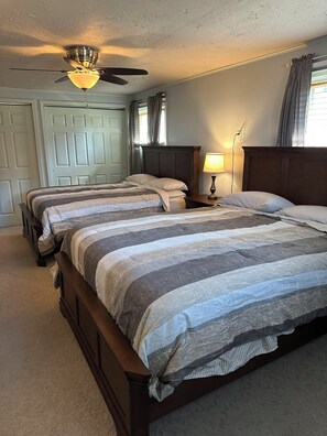 A bedroom with two beds, a ceiling fan, a nightstand with a lamp, and a window with curtains. - Lake Wisconsin Resort (Poynette)