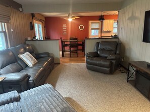 A living room with a leather sofa, a leather armchair, and a small table. There is a dining table with chairs in the background. - Lake Wisconsin Resort (Poynette)