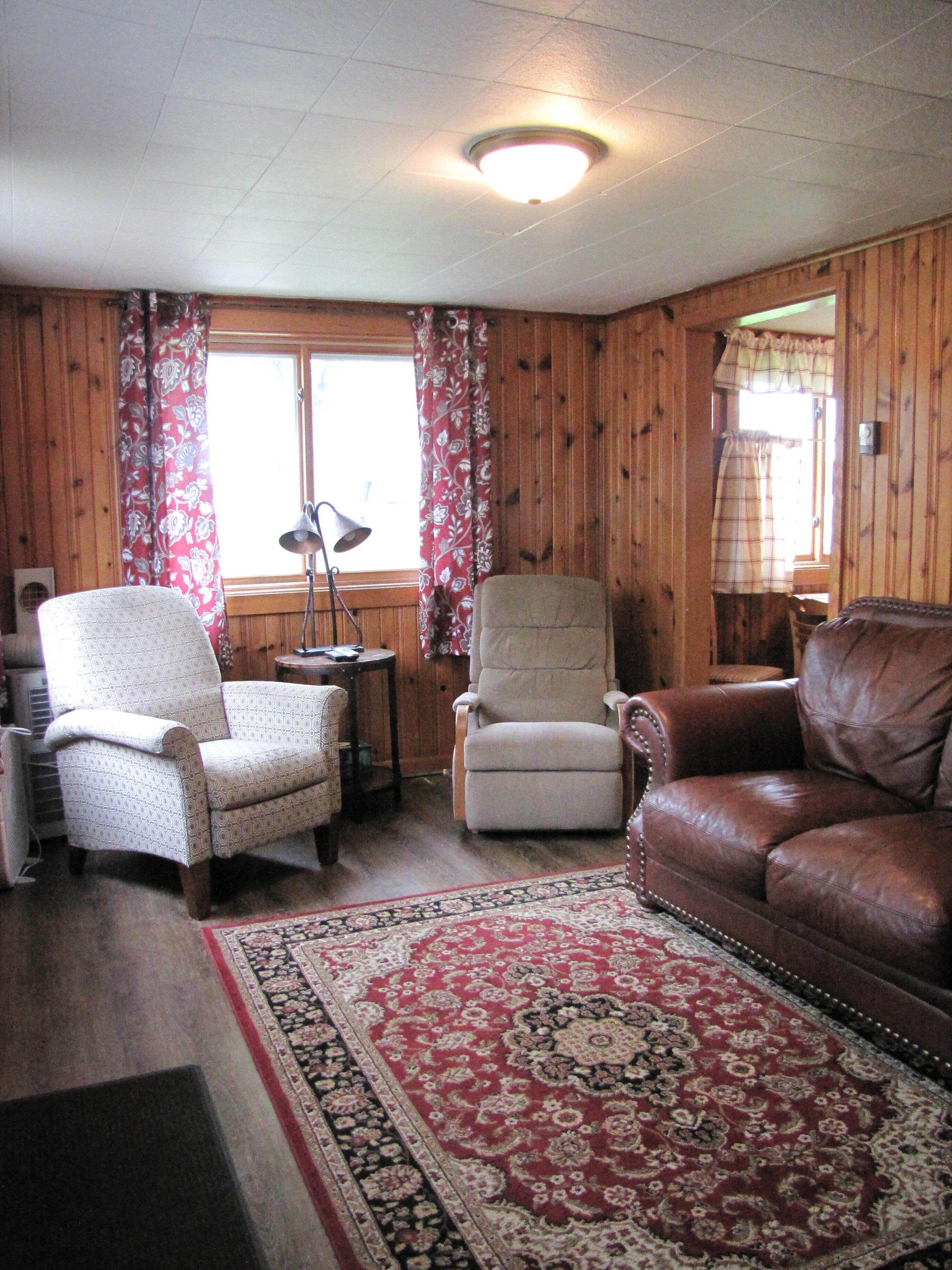 Una sala de estar con un sillón estampado, un sofá de cuero y un tapete rojo y blanco.