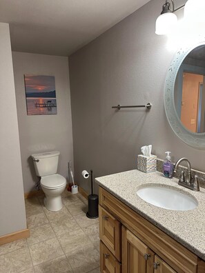 A bathroom with a toilet, sink, mirror, and a painting on the wall. - Lake Wisconsin Resort (Poynette)