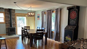 Uma área de refeições com mesa e cadeiras de madeira, mesa de futebol de mesa, alvo de dardos e lareira.