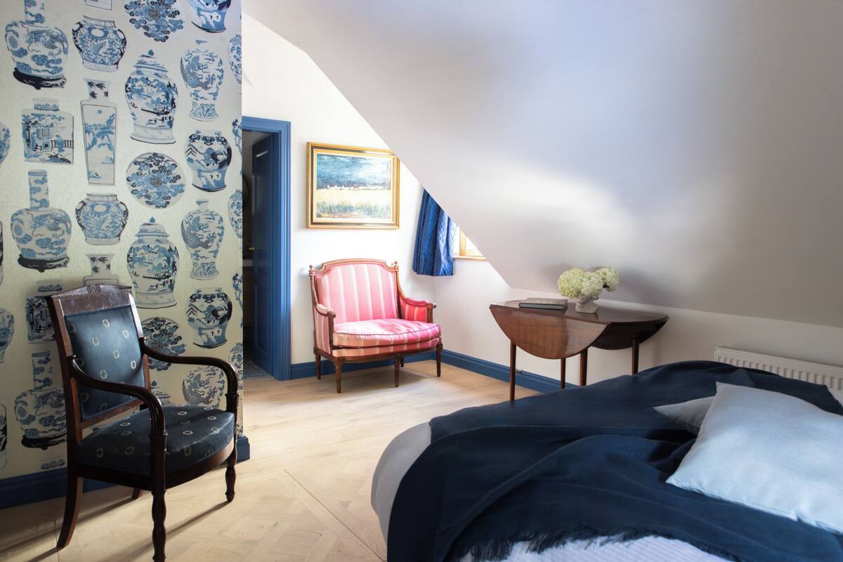 Ein Schlafzimmer mit einem Bett, einem Sessel, einem kleinen Tisch und einem Bild an der Wand.