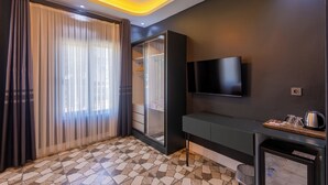 Ett modernt hotellrum med en stor skjutdörr i glas, en platt-TV som är monterad på väggen, ett litet pentry och ett klinkergolv med ett mönster.