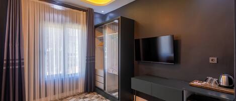 A modern hotel room with a large sliding glass door, a flat-screen TV mounted on the wall, a small kitchenette, and a patterned tile floor.