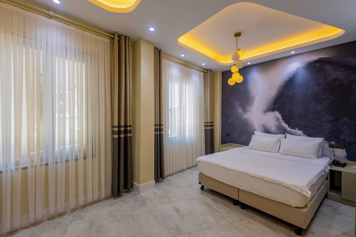 A modern bedroom with a large bed, a ceiling light fixture, and a wall mural.