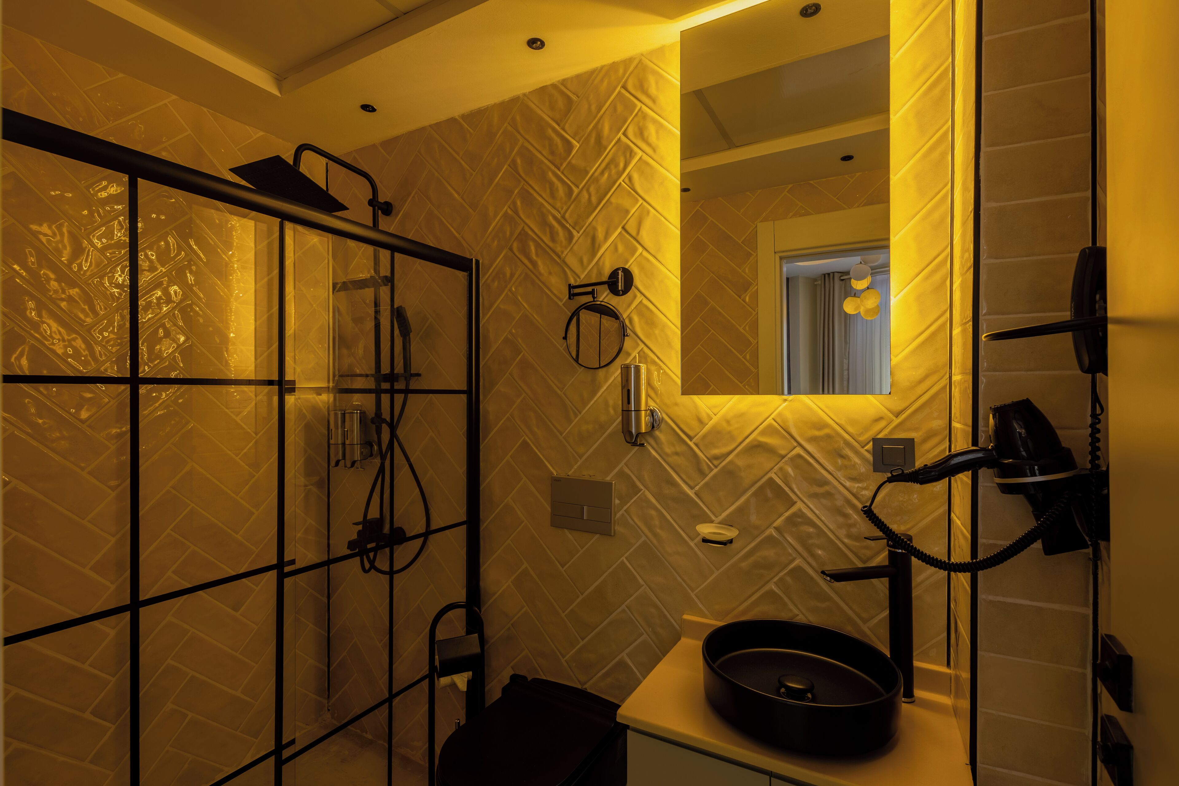 A bathroom with a herringbone-patterned tile wall, a glass shower enclosure, a round sink, and a mirror above the sink.