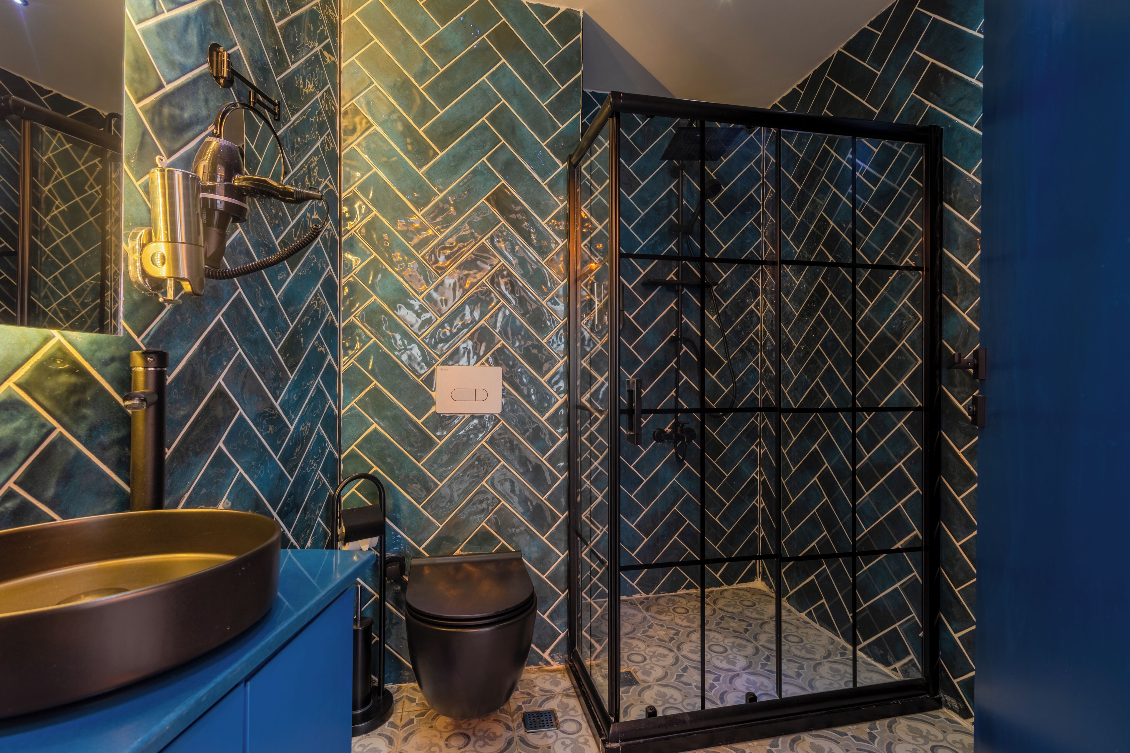 A bathroom with a herringbone tile pattern, a black shower enclosure, a round sink, and a toilet.
