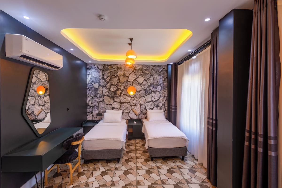A modern hotel room with two beds, a desk, and a stone accent wall.