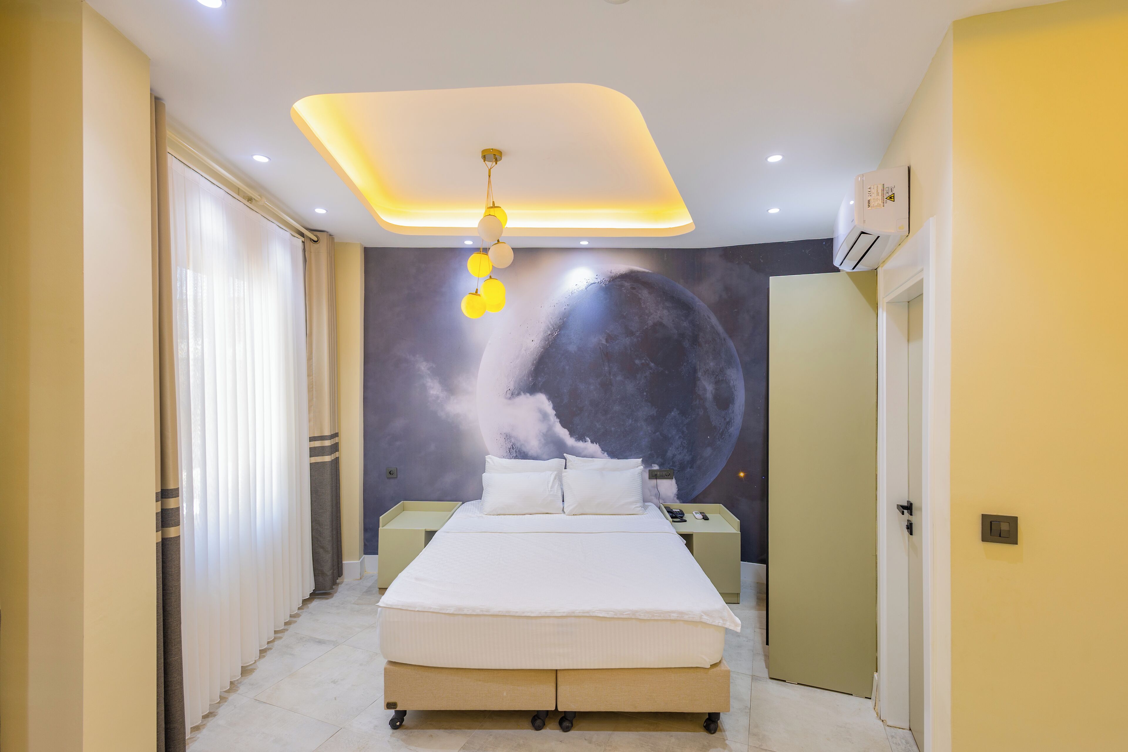 Un dormitorio con cama, mesitas de noche, un mural en la pared y una lámpara en el techo.