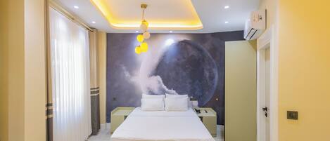 Un dormitorio con cama, mesitas de noche, un mural en la pared y una lámpara en el techo.